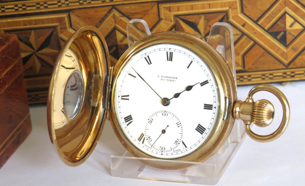 A 1930s gold-toned half hunter pocket watch displayed open, revealing a white dial with black Roman numerals and a subsidiary seconds dial.