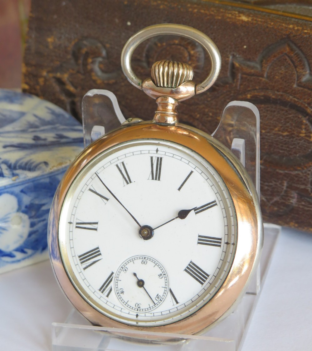 An open-face antique silver pocket watch featuring a white enamel dial, black Roman numerals, a sub-seconds dial, and rose gold accents around the bezel and crown bow.