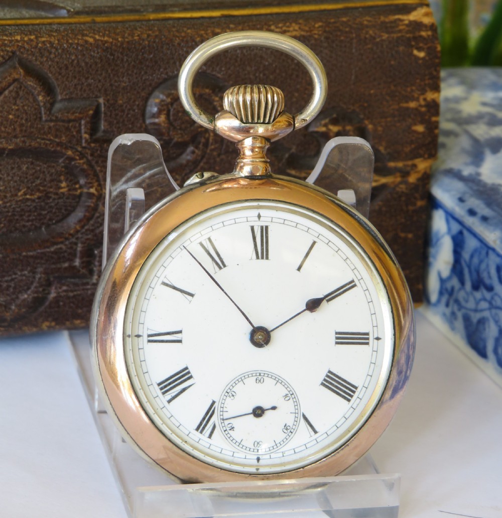 An open-face antique silver pocket watch featuring a white enamel dial, black Roman numerals, a sub-seconds dial, and rose gold accents around the bezel and crown bow. View II