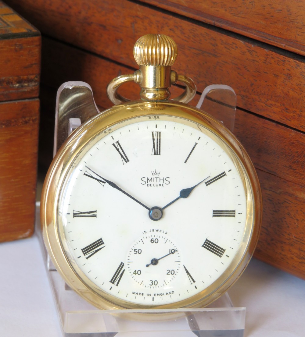 A gold-toned open-faced Smiths De Luxe pocket watch featuring a white dial with Roman numerals and a subsidiary seconds dial. View II