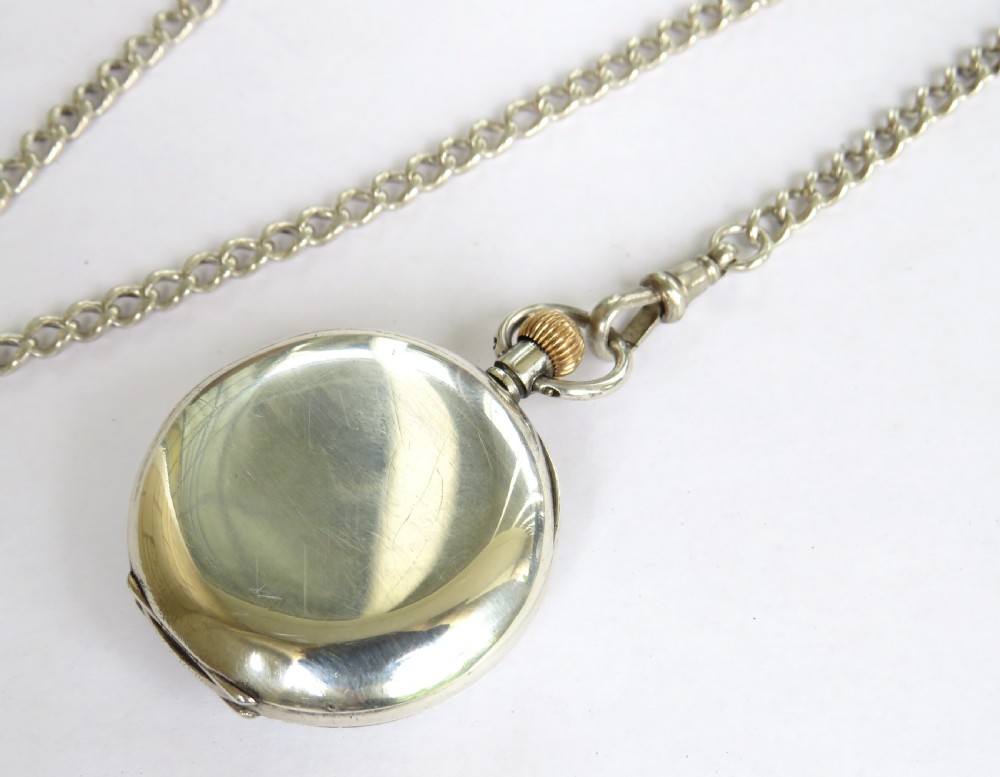 An open-face silver pocket watch with a white enamel dial, Roman numerals, a subsidiary seconds sub-dial, and an attached silver chain with a T-bar. View V