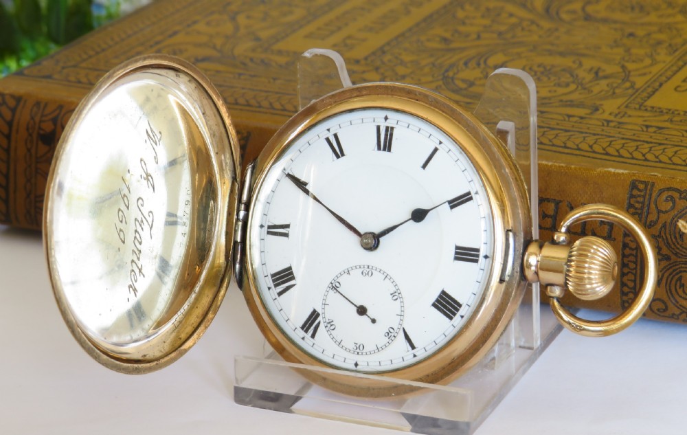 An opened gold antique full hunter pocket watch displaying a white enamel dial with black Roman numerals and a subsidiary seconds dial.