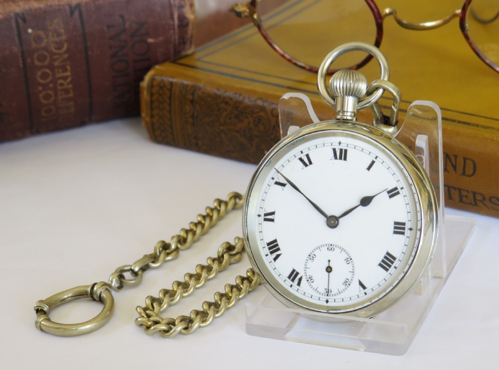 An open face silver pocket watch featuring black Roman numerals on a white enamel dial with an attached brass curb chain.
