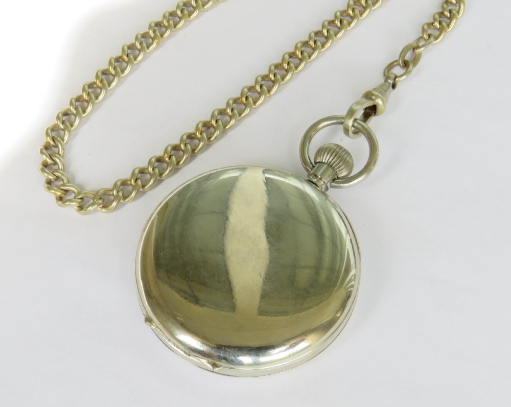 An open face silver pocket watch featuring black Roman numerals on a white enamel dial with an attached brass curb chain. View VI