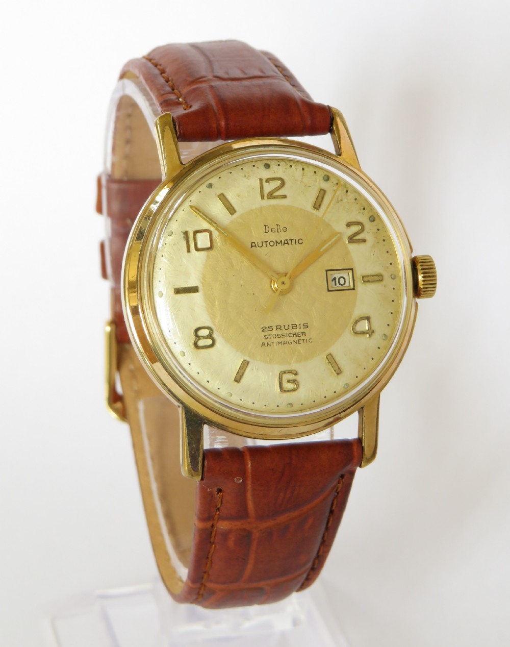 A 1950s gents gold-toned automatic wristwatch featuring a textured dial, Arabic numerals, a date window at 3 oclock, and a brown leather strap. View II