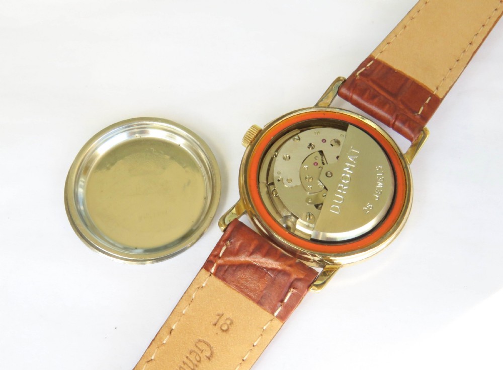 A 1950s gents gold-toned automatic wristwatch featuring a textured dial, Arabic numerals, a date window at 3 oclock, and a brown leather strap. View III