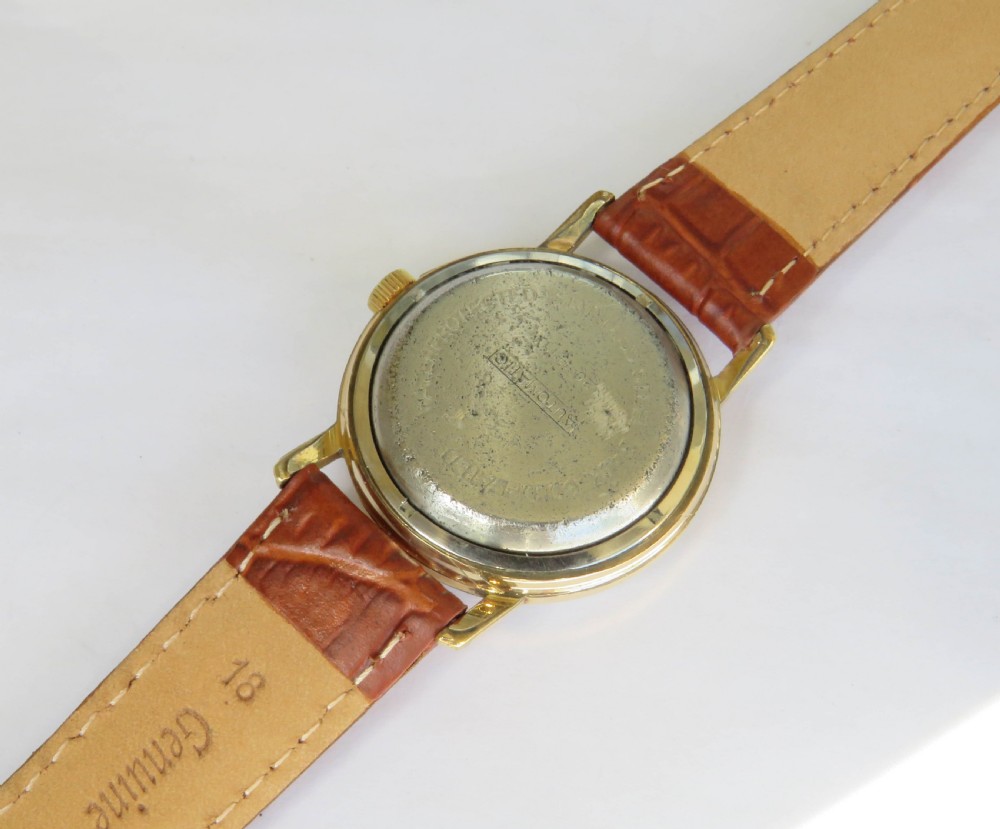 A 1950s gents gold-toned automatic wristwatch featuring a textured dial, Arabic numerals, a date window at 3 oclock, and a brown leather strap. View IV