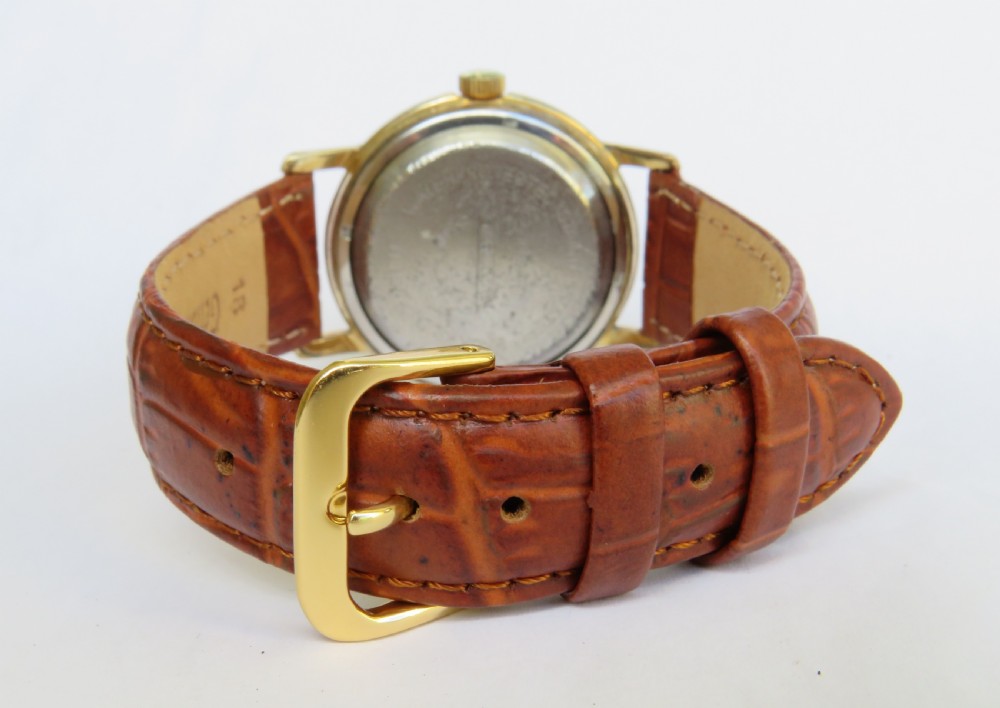 A 1950s gents gold-toned automatic wristwatch featuring a textured dial, Arabic numerals, a date window at 3 oclock, and a brown leather strap. View V