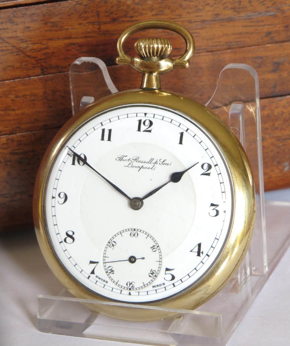A gold-toned open-face pocket watch featuring a white enamel dial with black Arabic numerals and a sub-seconds dial.
