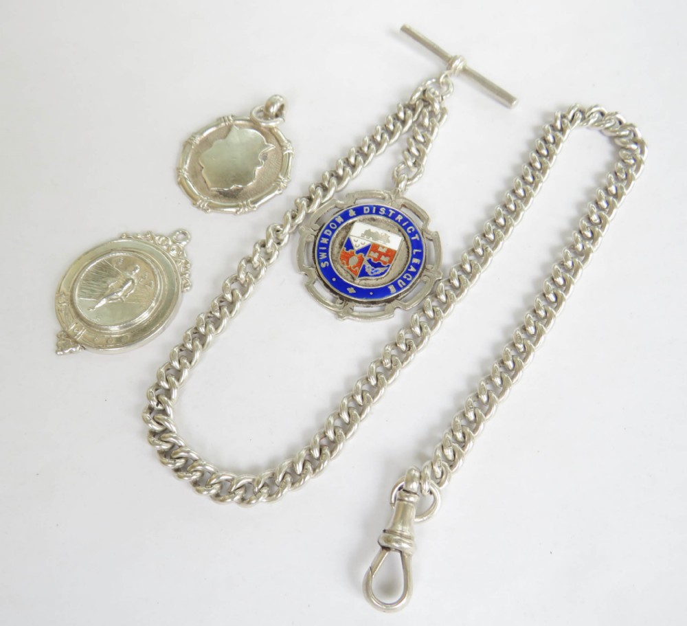 An Edwardian sterling silver curb link watch chain featuring a T-bar, swivel clasp, and an enamel medallion fob accompanied by two silver sporting medals.