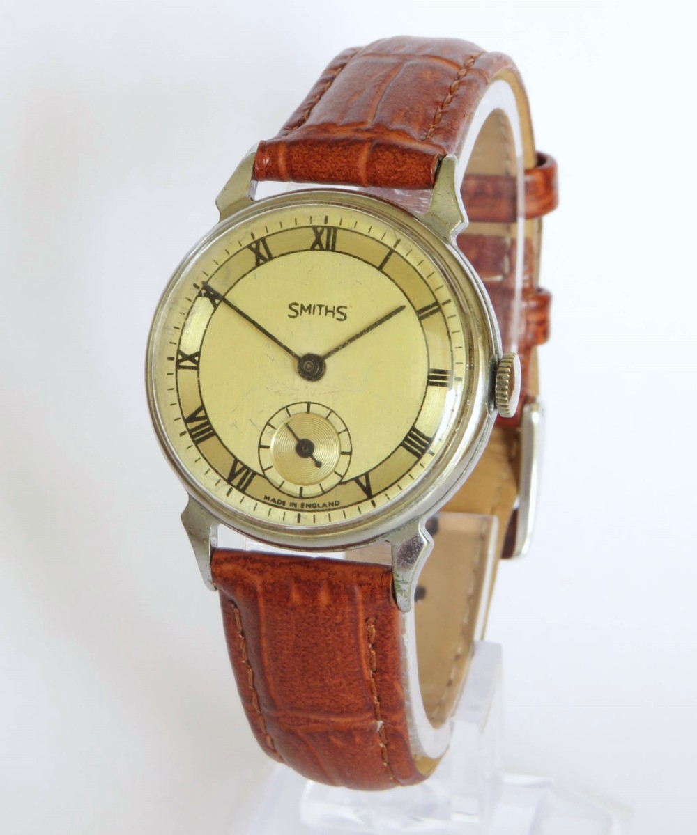 A mid-20th-century gents Smiths wristwatch featuring a champagne dial with Roman numerals, subsidiary seconds dial, silver-tone case, and tan leather strap.