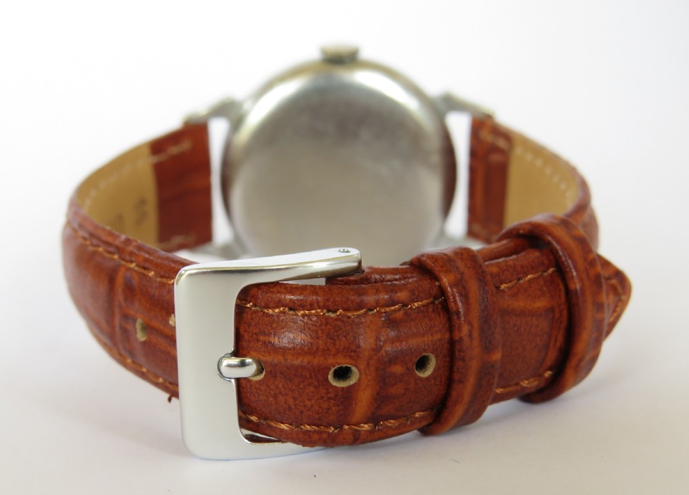 A mid-20th-century gents Smiths wristwatch featuring a champagne dial with Roman numerals, subsidiary seconds dial, silver-tone case, and tan leather strap. View V