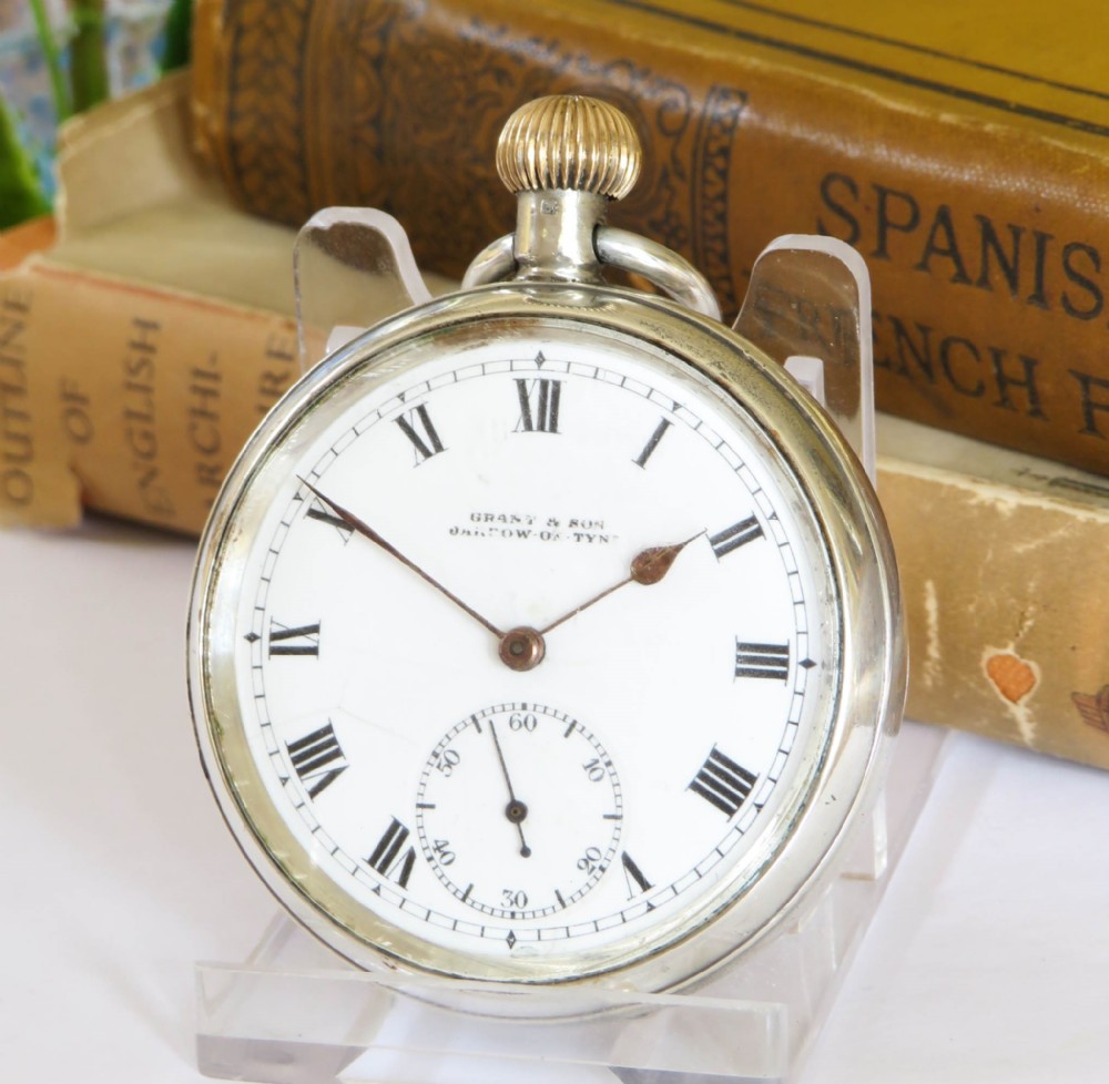 An antique open-face silver pocket watch featuring a white enamel dial with black Roman numerals and a small seconds sub-dial at six oclock.