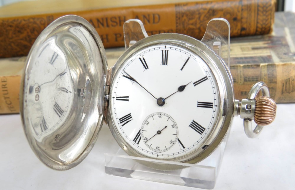 A silver full hunter pocket watch shown open to display a white enamel dial with black Roman numerals and a small seconds sub-dial.