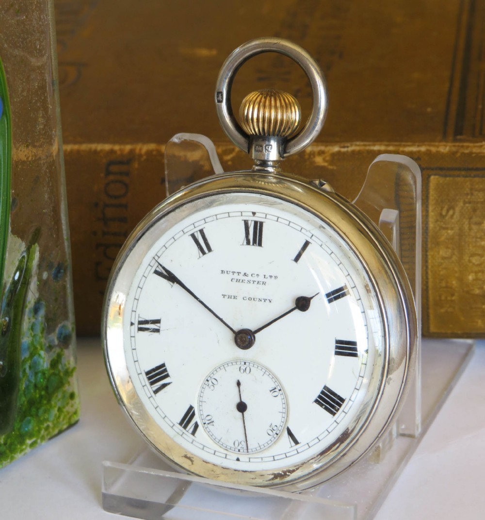 An open-face antique silver pocket watch featuring a white enamel dial with black Roman numerals and a subsidiary seconds sub-dial.
