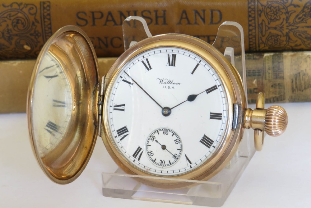 An open gold-toned full hunter pocket watch displaying a white enamel dial with black Roman numerals and a subsidiary seconds dial.