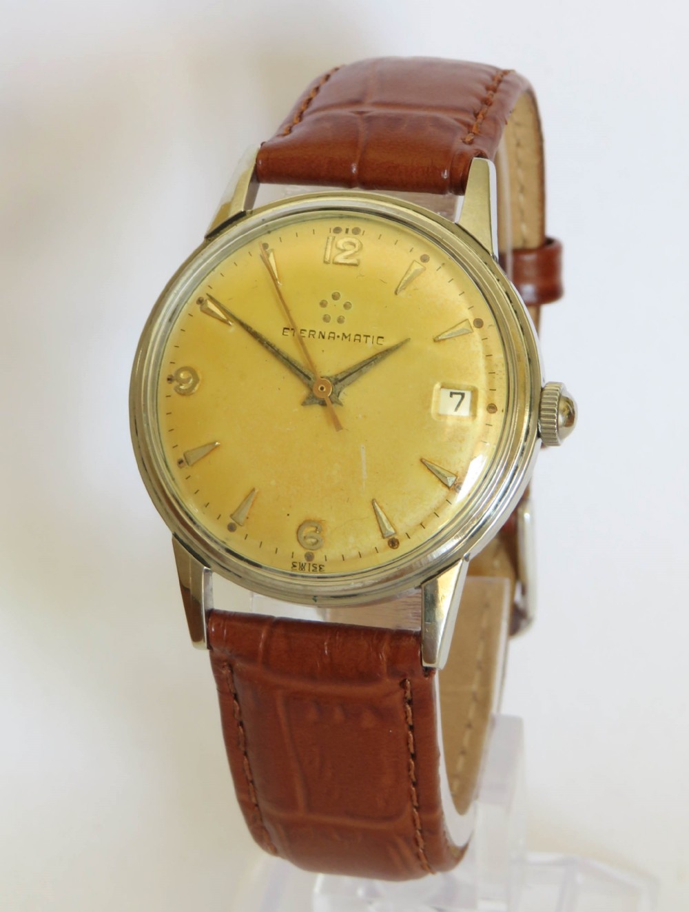A 1950s Eterna-Matic gents wrist watch featuring a champagne dial, gold-tone hour markers, date aperture, and a brown leather strap.