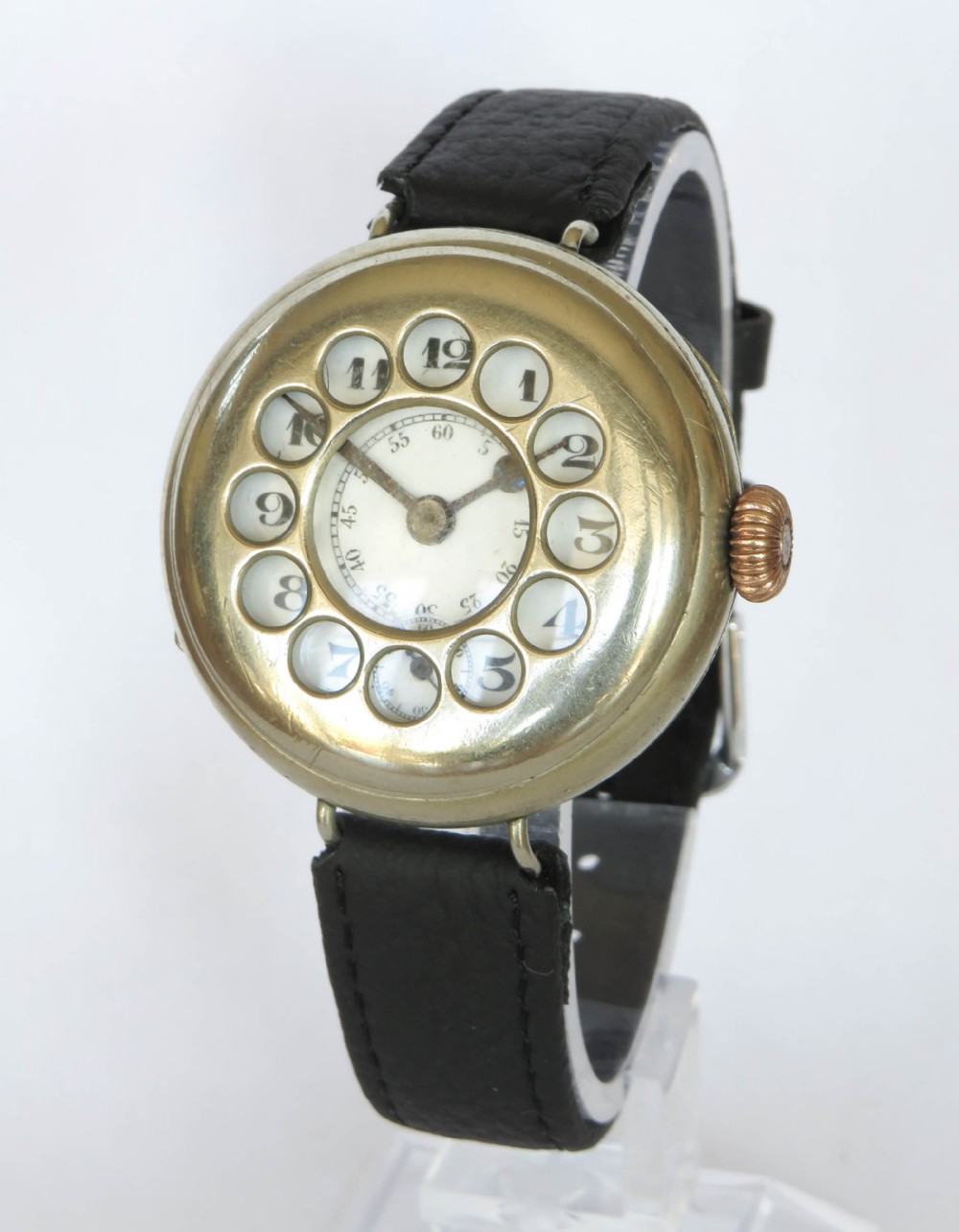 A military trench watch featuring a polished metal shrapnel guard with circular hour cutouts over a white enamel dial with a black leather strap.
