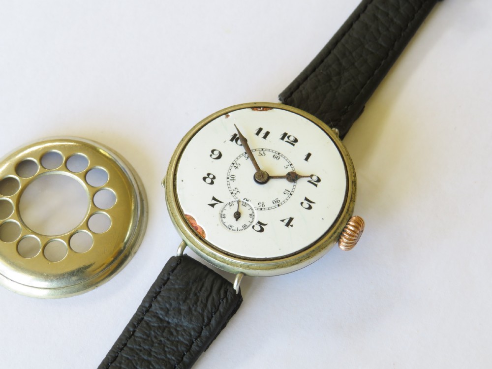 A military trench watch featuring a polished metal shrapnel guard with circular hour cutouts over a white enamel dial with a black leather strap. View III
