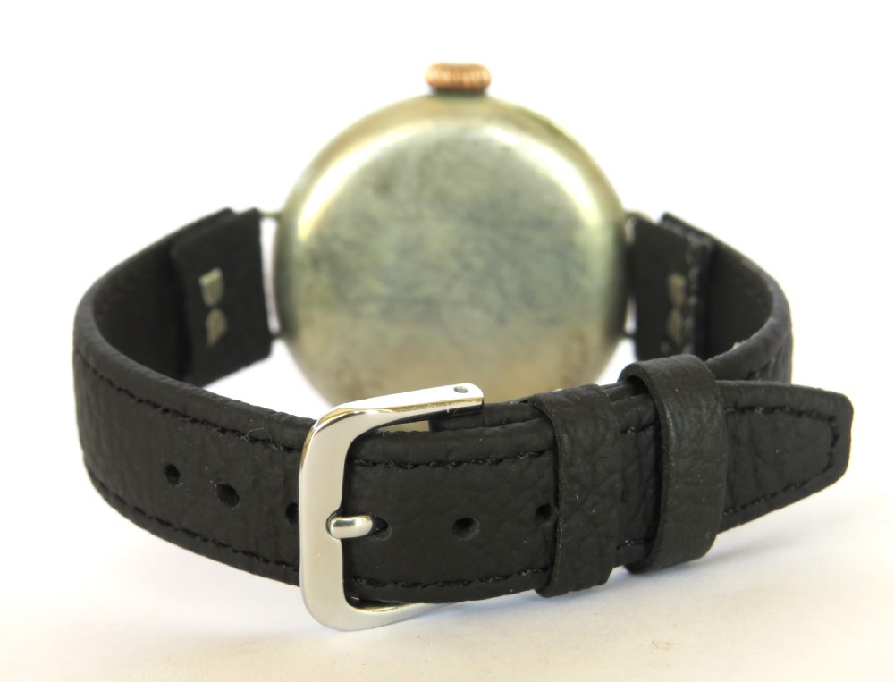 A military trench watch featuring a polished metal shrapnel guard with circular hour cutouts over a white enamel dial with a black leather strap. View VII