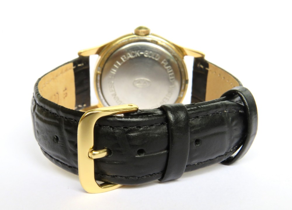 A 1950s gents Berg Parat wristwatch featuring a gold-plated case, a black dial with gold numerals, and a black leather strap. View V