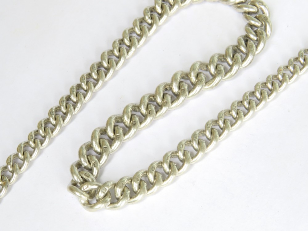 An Edwardian sterling silver Albert pocket watch chain featuring curb links, a T-bar fastener, a swivel clasp, and a decorative shield-shaped fob with a rose gold cartouche. View V