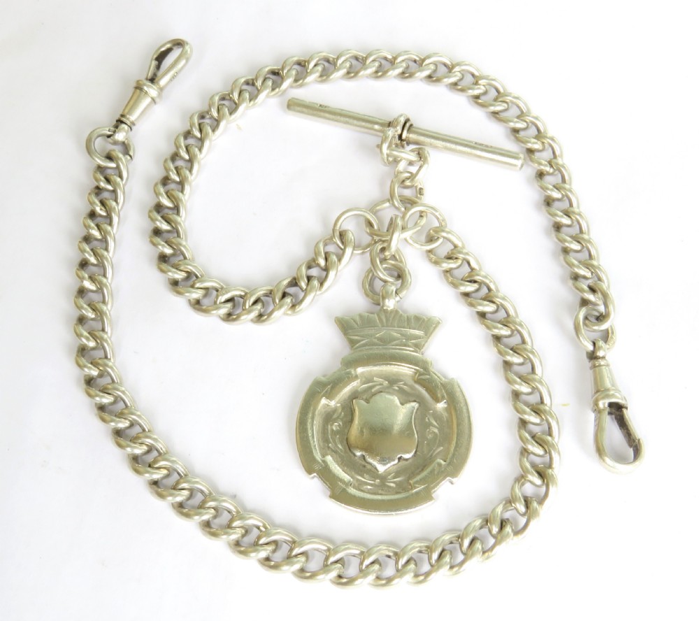 An antique sterling silver double Albert pocket watch chain featuring curb links, two swivel clasps, a central T-bar, and an engraved shield fob medallion topped with a crown motif.