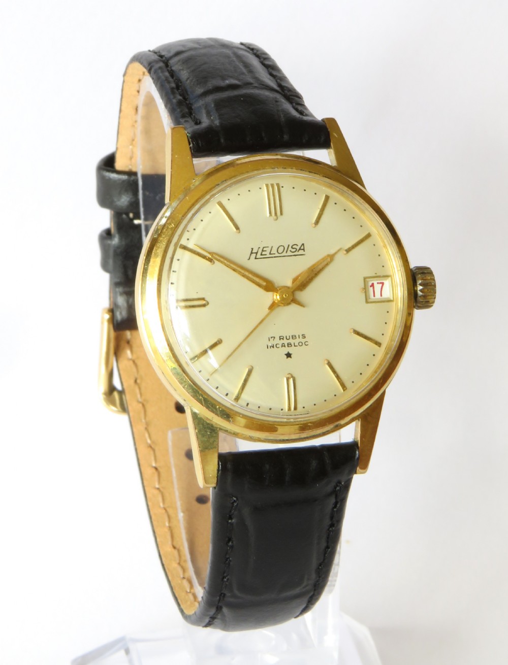 A 1950s gents Heloisa wrist watch with a circular gold-tone case, cream dial with gold baton markers, date aperture at three oclock, and black leather strap. View II