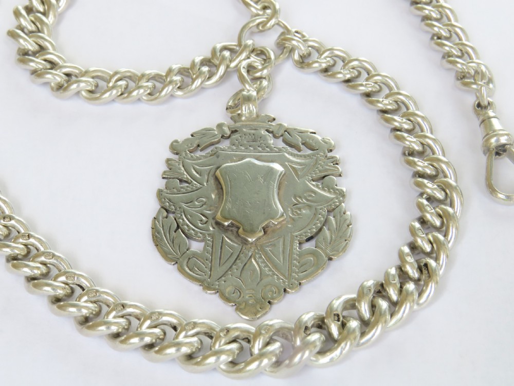 An antique silver double Albert pocket watch chain featuring curb links, two swivel dog clips, a central T-bar, and a decorative shield-shaped pendant fob. View II