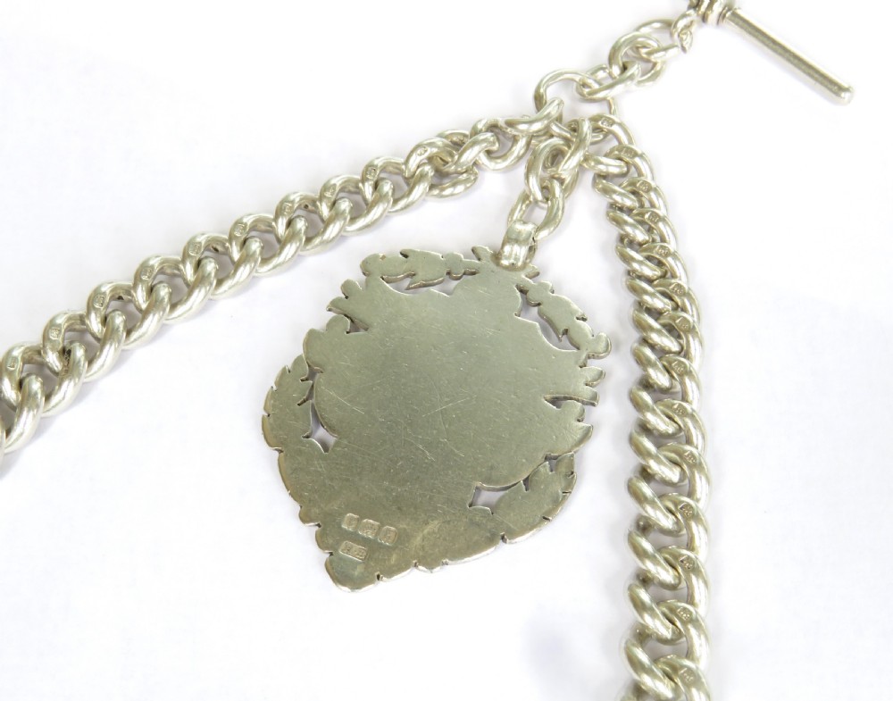 An antique silver double Albert pocket watch chain featuring curb links, two swivel dog clips, a central T-bar, and a decorative shield-shaped pendant fob. View III