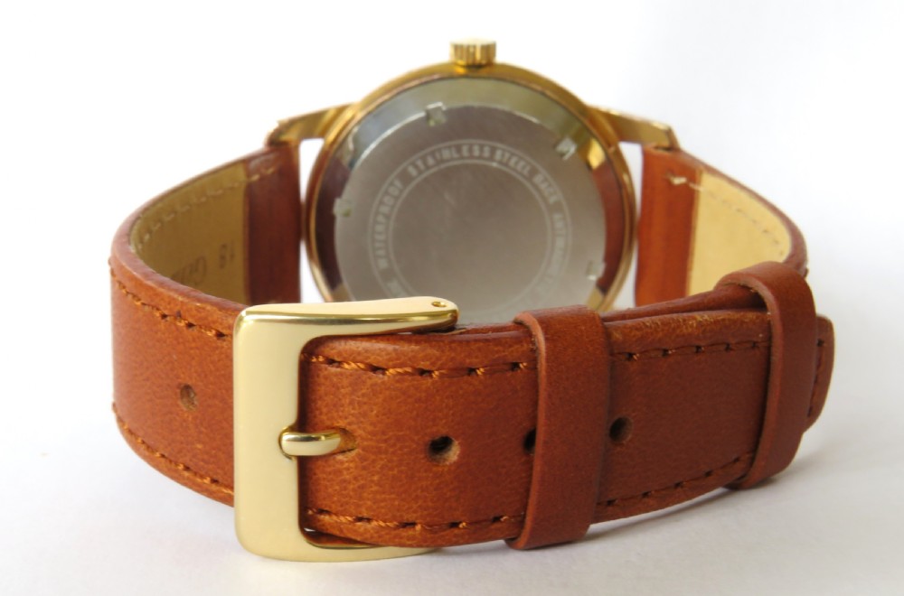A 1950s gentlemens Ramona automatic wristwatch featuring a gold-plated case, cream dial with arrow-shaped markers, and a stitched tan leather strap. View V