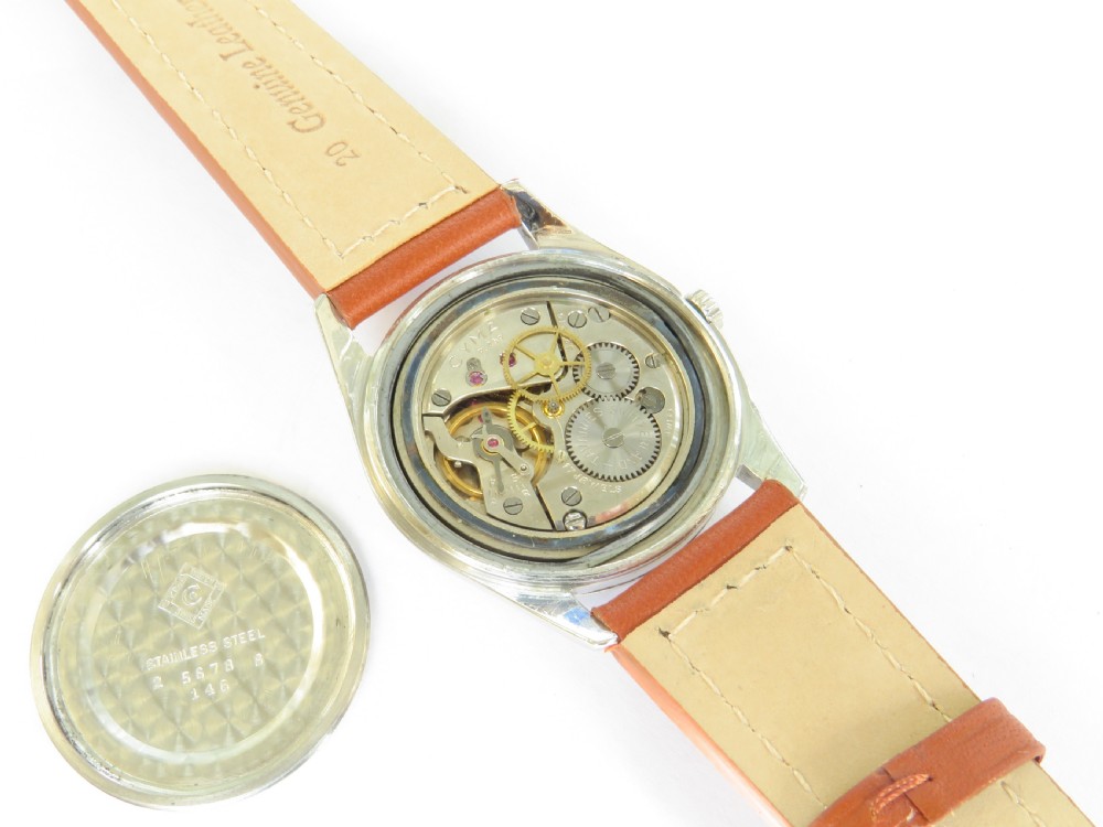 A 1960s Cyma Navystar wristwatch featuring a black dial with gold-toned markers and hands, housed in a polished metal case on a tan leather strap. View II