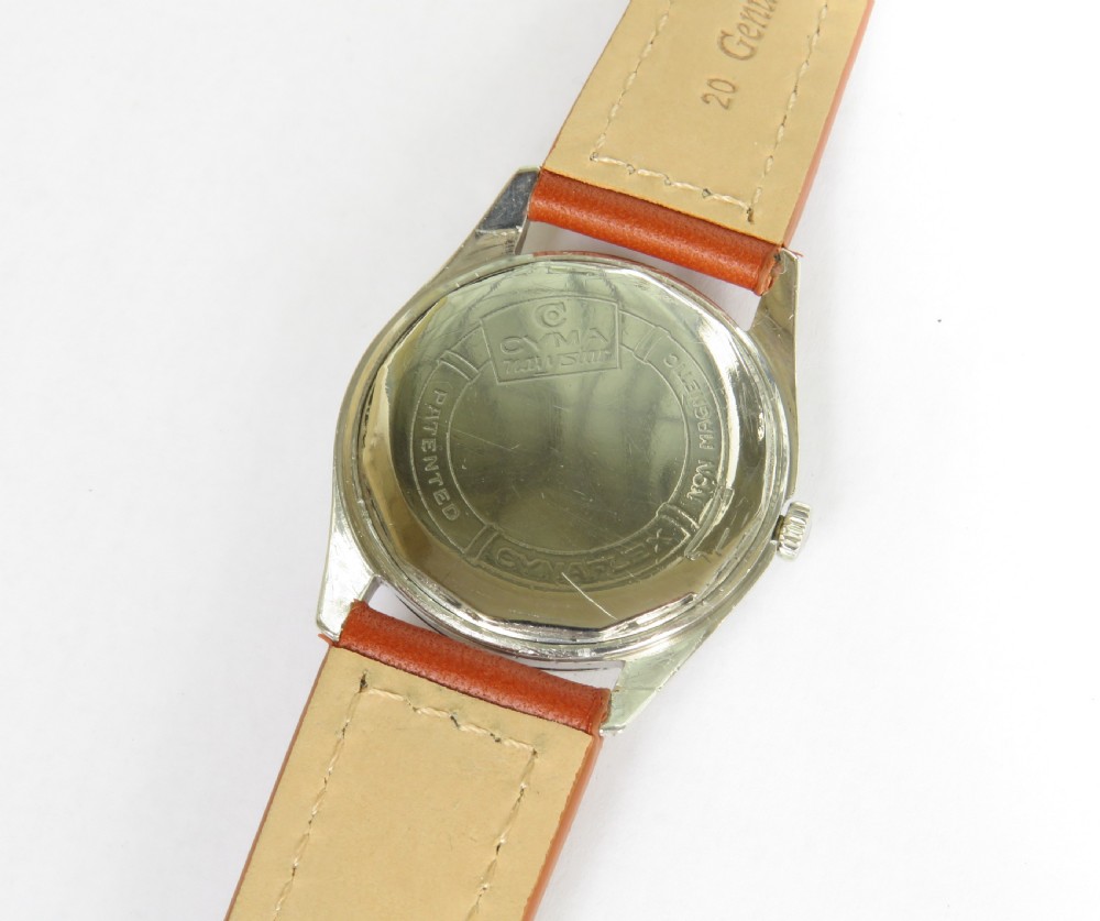 A 1960s Cyma Navystar wristwatch featuring a black dial with gold-toned markers and hands, housed in a polished metal case on a tan leather strap. View III