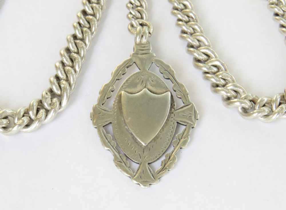 A sterling silver double Albert watch chain featuring curb links, two swivel clips, a central T-bar, and a shield-shaped silver fob. View II
