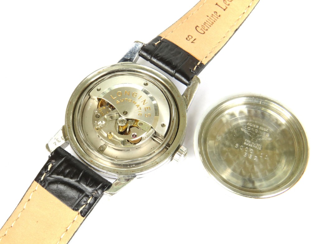 A 1957 Longines Conquest automatic wristwatch featuring a stainless steel case, patinated cream dial, gold-tone hour markers, and a black leather strap. View III