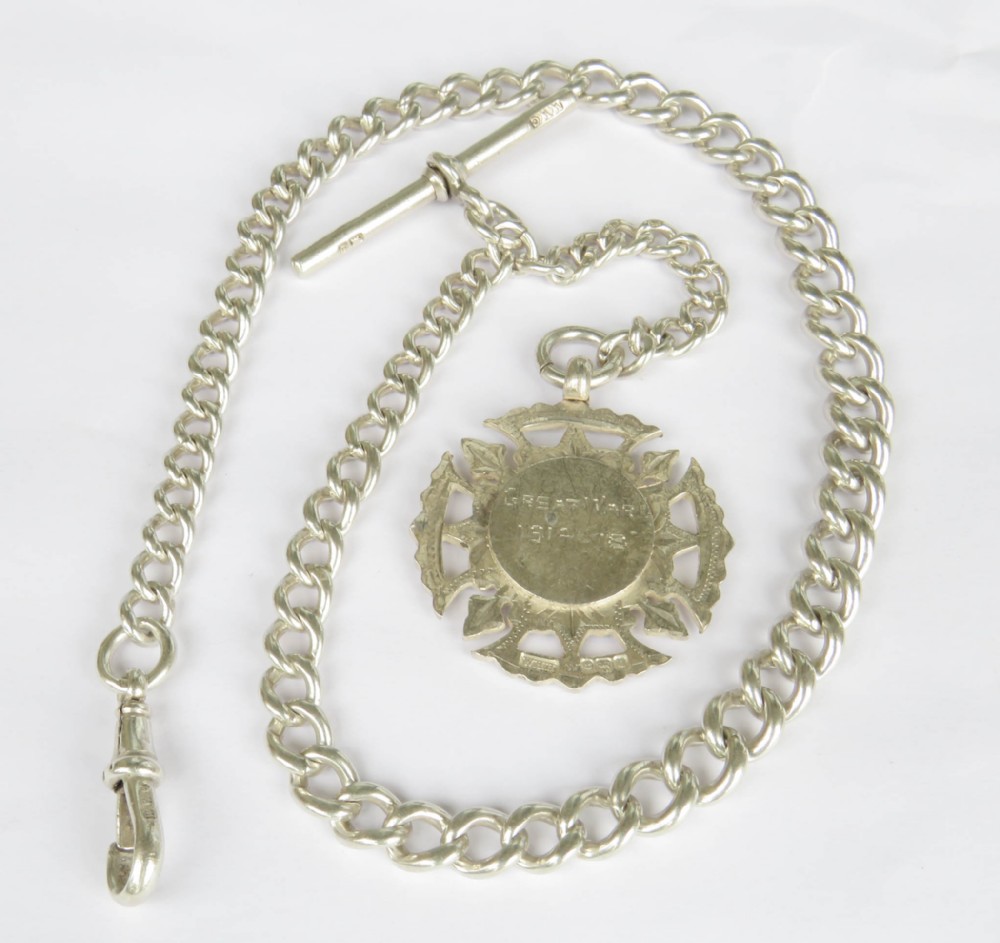 A sterling silver curb link Albert pocket watch chain featuring a T-bar, swivel clasp, and a carved Great War 1914-1918 medallion fob.
