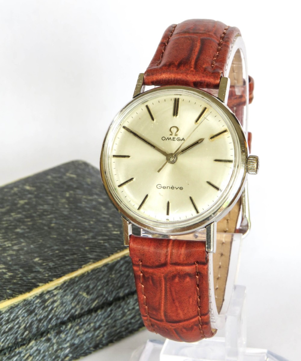 A 1966 Omega Geneve wristwatch featuring a round silver-toned dial, black baton indices, and a textured brown leather strap.