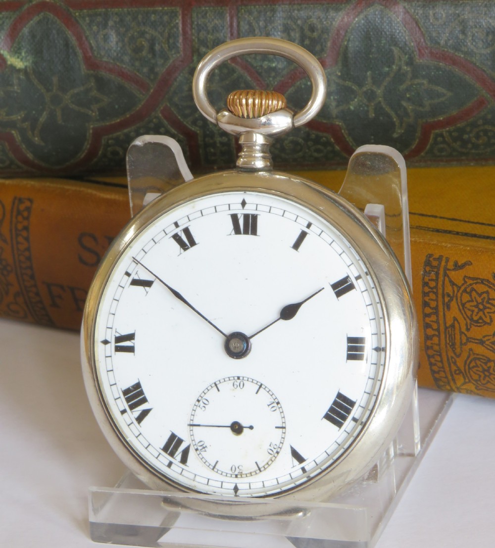 An antique open-face silver pocket watch featuring a white enamel dial with black Roman numerals and a small sub-seconds dial.