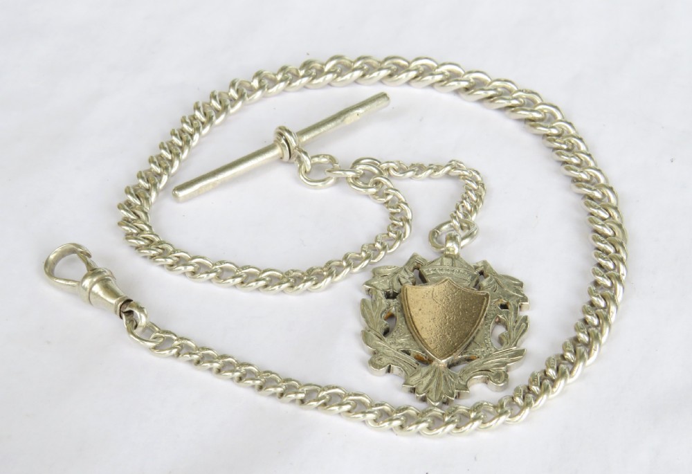 An antique sterling silver curb link Albert watch chain featuring a T-bar, swivel clasp, and a central shield-shaped decorative fob.