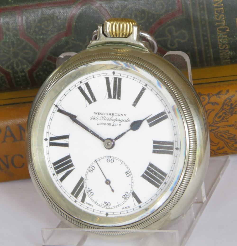 An open-face pocket watch featuring a white enamel dial with black Roman numerals, blued steel hands, a subsidiary seconds dial, and a silver-toned metal case with a gold-coloured winding crown.