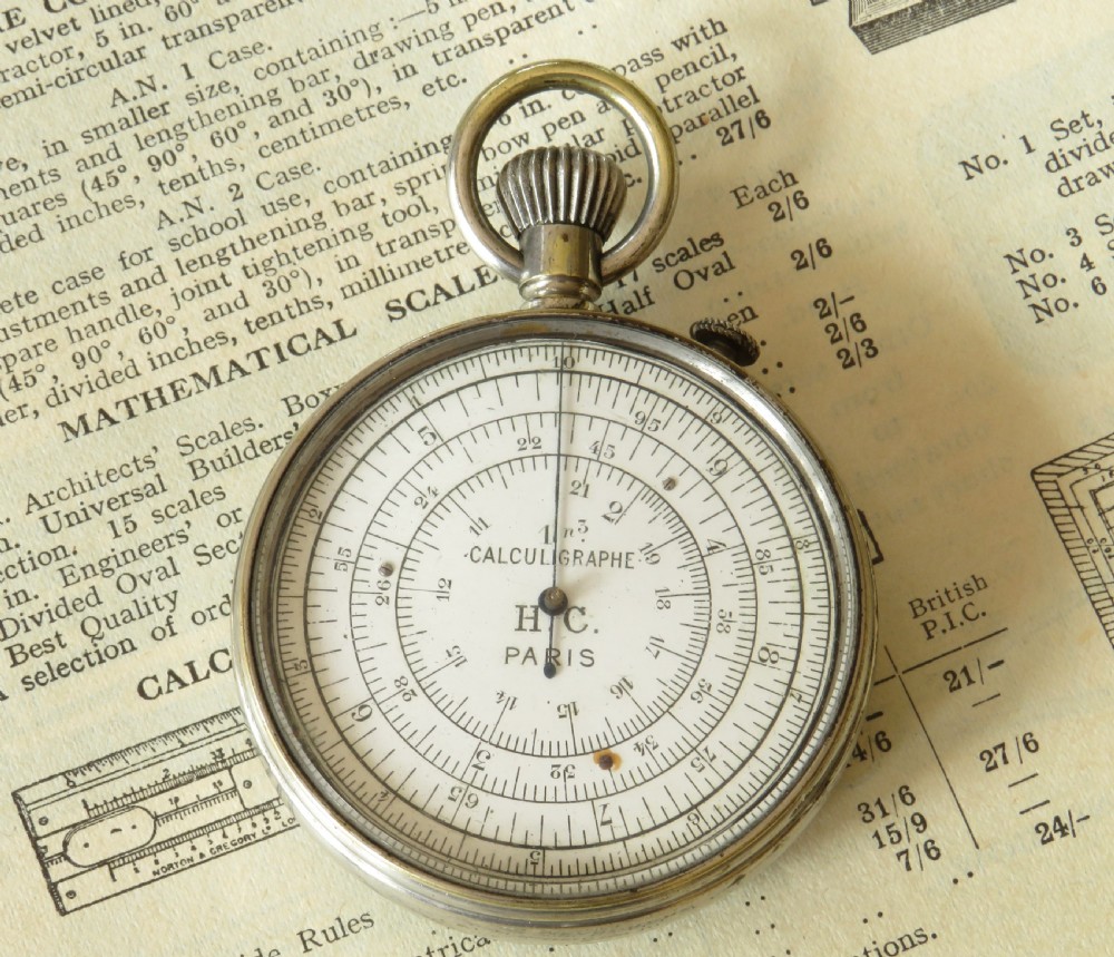 A pocket watch styled mechanical circular slide rule with a nickel case, white dial featuring concentric scales, and text reading Calculigraphe H.C. Paris.