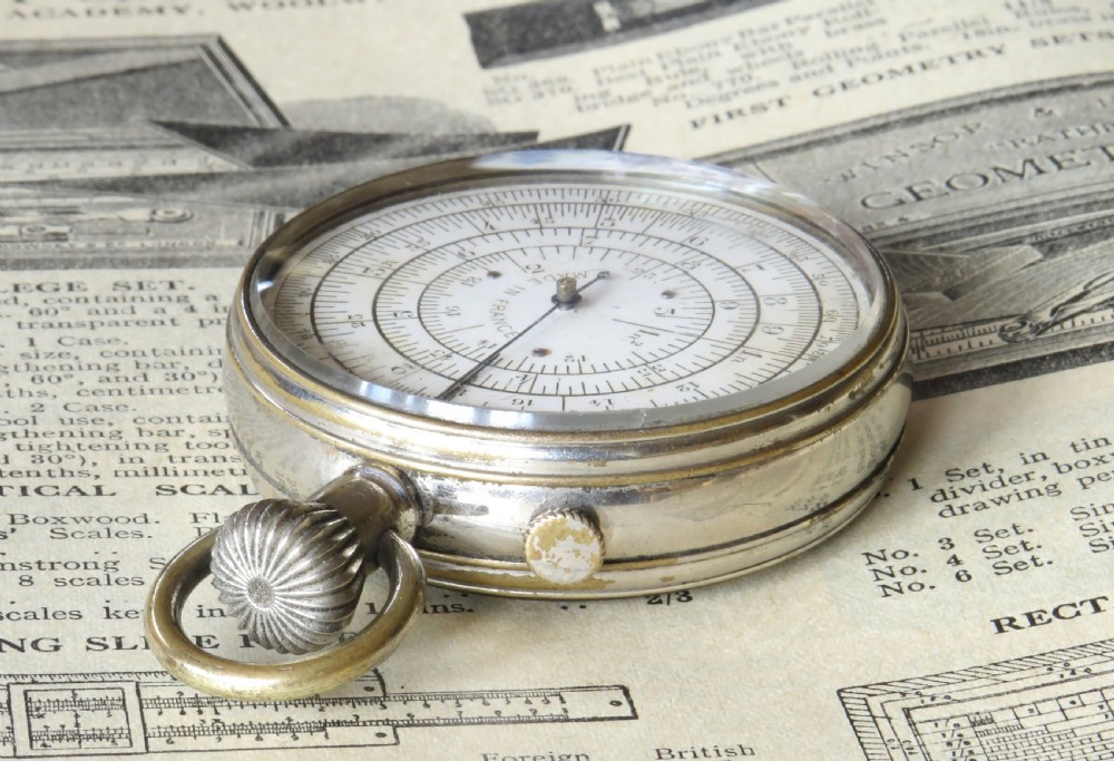 A pocket watch styled mechanical circular slide rule with a nickel case, white dial featuring concentric scales, and text reading Calculigraphe H.C. Paris. View III
