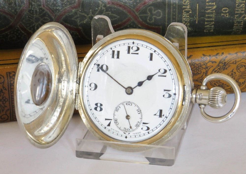 A 1930s silver hunter pocket watch featuring a open hinged cover, a white enamel dial with black Arabic numerals, and a sub-seconds display at six oclock.