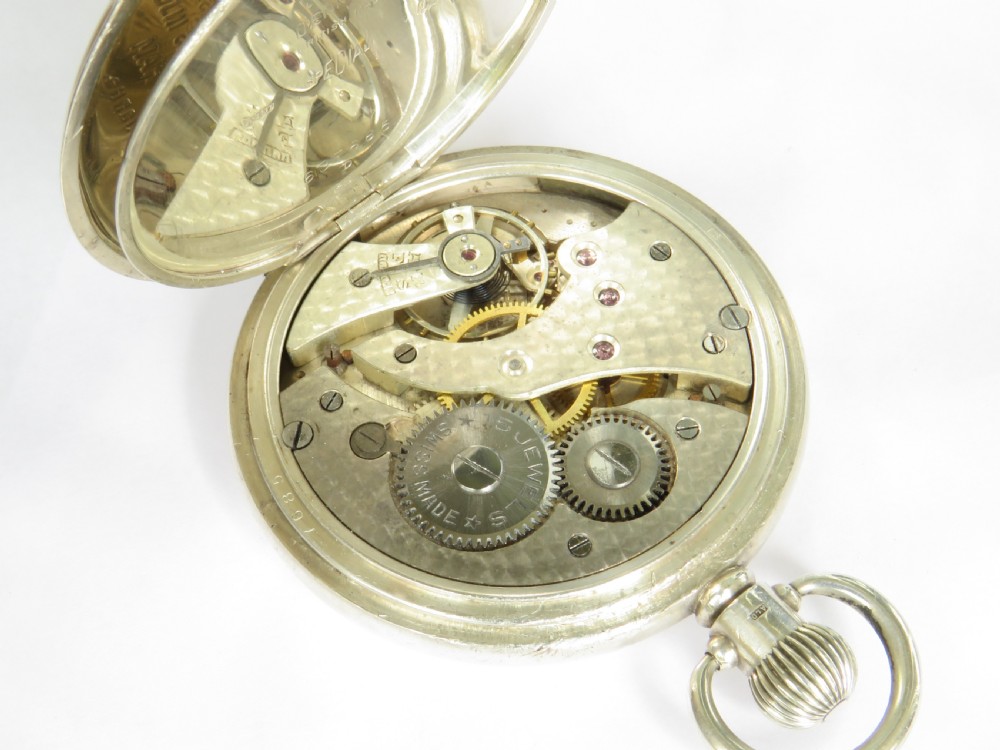 A 1930s silver hunter pocket watch featuring a open hinged cover, a white enamel dial with black Arabic numerals, and a sub-seconds display at six oclock. View VI