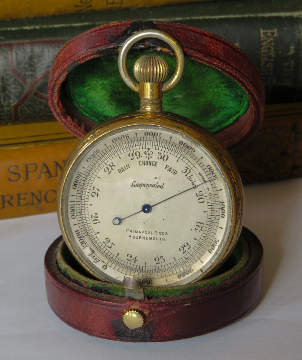 An antique brass pocket barometer and altimeter shown inside an open burgundy leather travel case lined with green velvet.