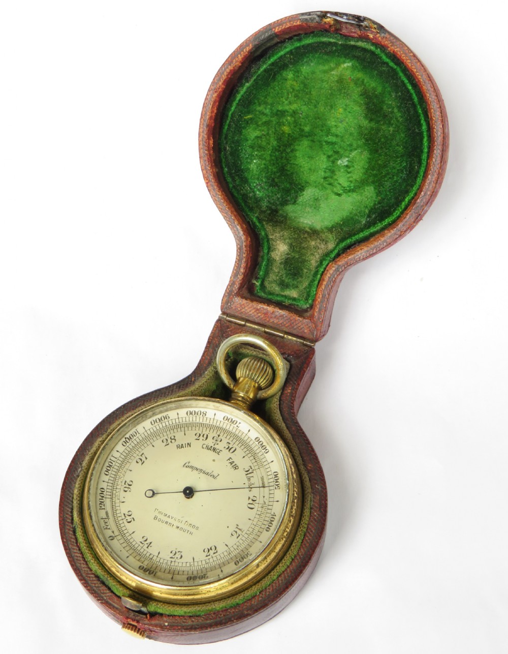 An antique brass pocket barometer and altimeter shown inside an open burgundy leather travel case lined with green velvet. View II