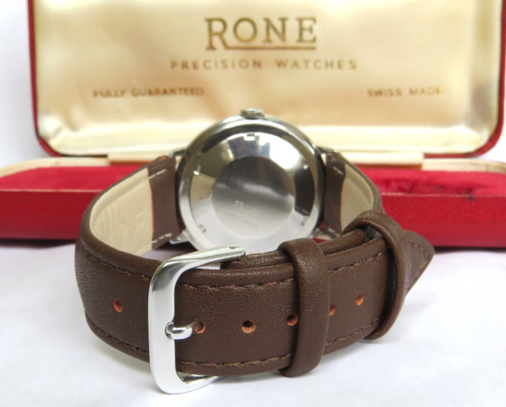 A 1960s mens Rone automatic wristwatch featuring a champagne dial, gold-tone casing, and a brown leather strap. View V