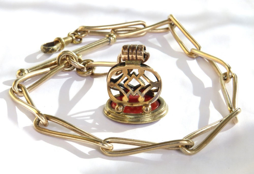 An antique 1920s rolled rose gold watch Albert chain featuring elongated trombone links, a T-bar, swivel clasp, and a carved carnelian fob pendant. View II