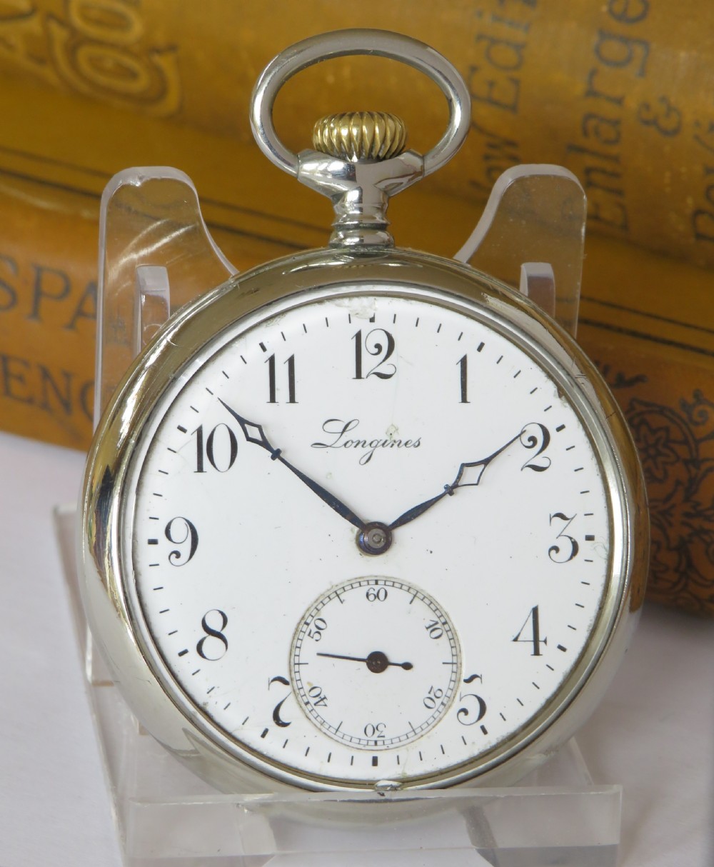 An antique open face Longines pocket watch featuring a white enamel dial with black Arabic numerals, a sub-seconds dial, and a silver casing with a brass crown. View II