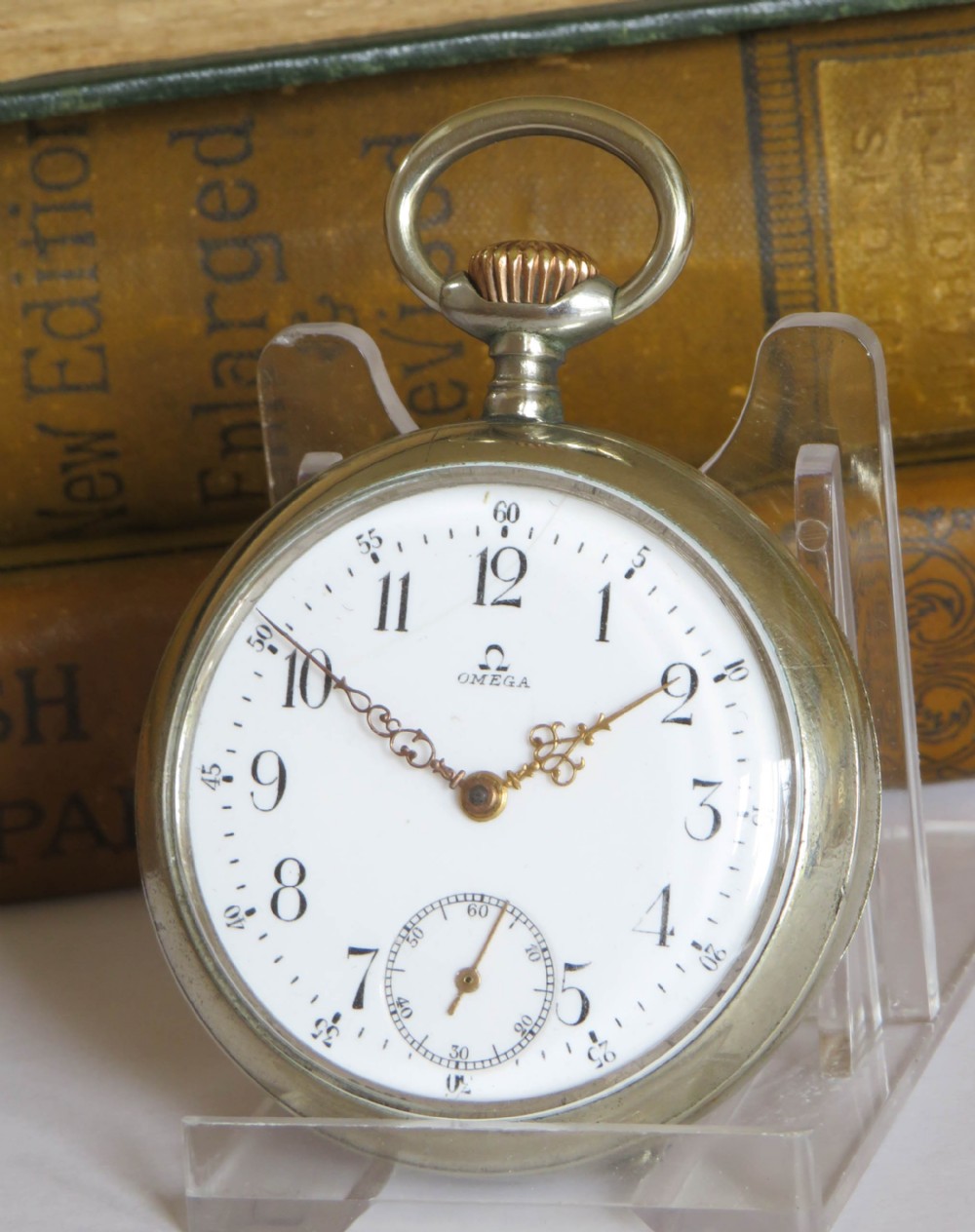 An open-face antique Omega pocket watch with a white enamel dial, black Arabic numerals, ornate hands, and a silver-toned metal case.